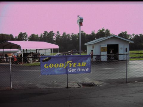 1992 Ford Mustang - A silver sedan is visible behind a fence and a Goodyear banner at an outdoor facility.
