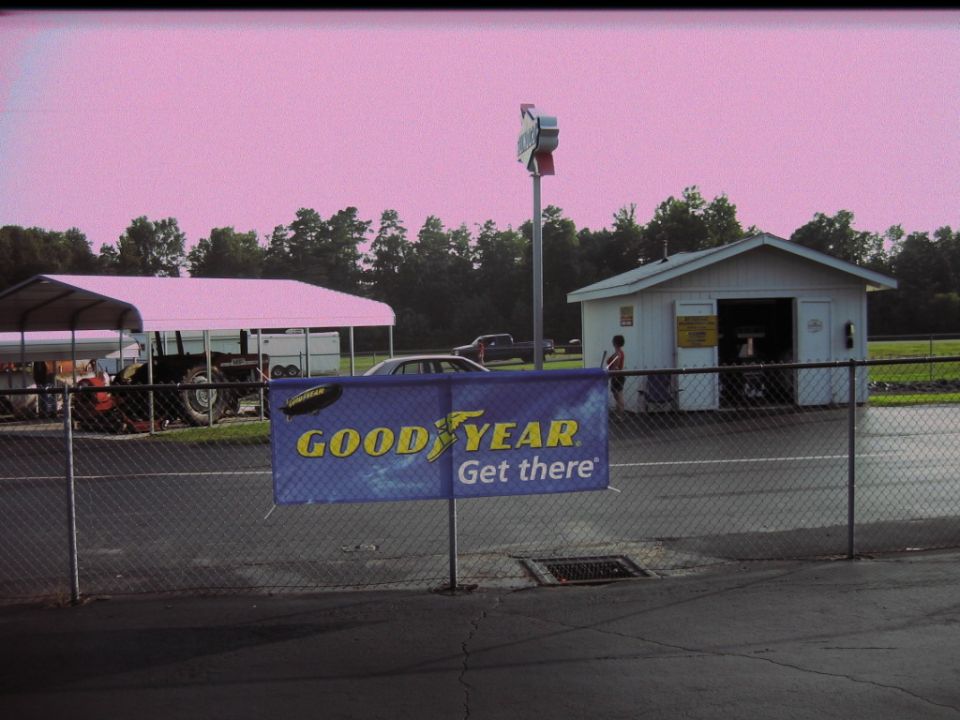 Silver sedan parked behind a fence with a Goodyear banner