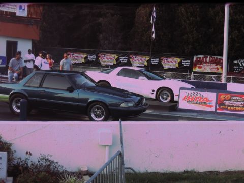 1992 Ford Mustang - Two cars are lined up at a drag strip, ready for a race. The dark green car is in the foreground.