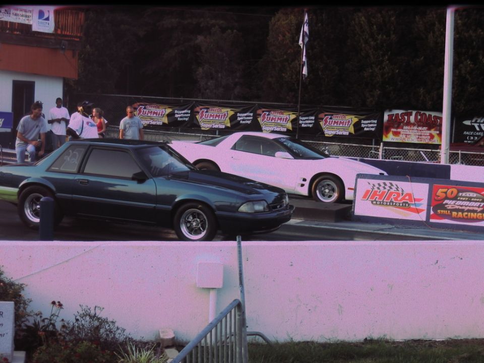 Dark green coupe and white coupe at drag strip starting line, people watching