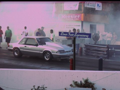 1992 Ford Mustang - A silver coupe drag car sits on the track with smoke in the background and spectators watching.