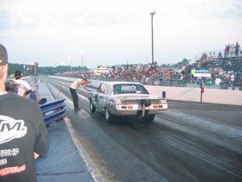 1992 Ford Mustang - A drag racing car is on the track, with a person leaning over its side. Spectators watch from the stands.