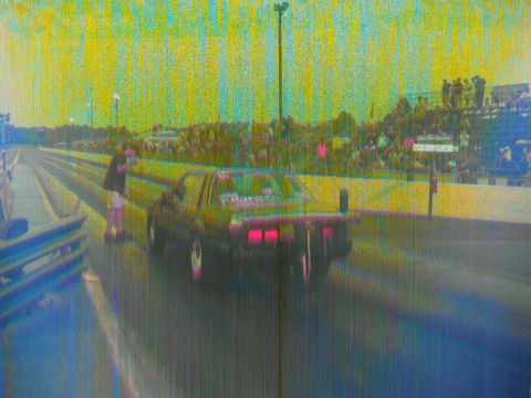 1992 Ford Mustang - A drag car speeds down the track with spectators watching from the stands.