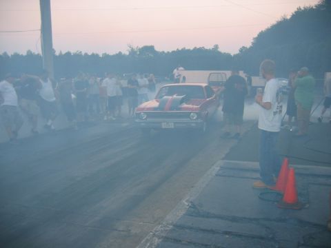 1992 Ford Mustang - A red drag car creates a cloud of smoke during a burnout on a race track as spectators watch.