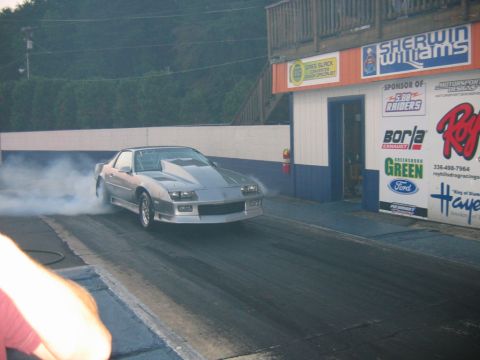 1992 Ford Mustang - A silver third-generation Chevrolet Camaro performs a burnout on a drag strip, with sponsor banners visible in the background.