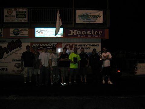 1992 Ford Mustang - A group of people are gathered at a drag strip at night, with various sponsor signs visible in the background.