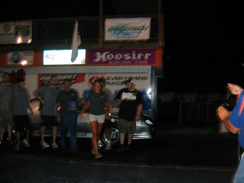 group of people standing in front of a trailer at night, with racing banners overhead