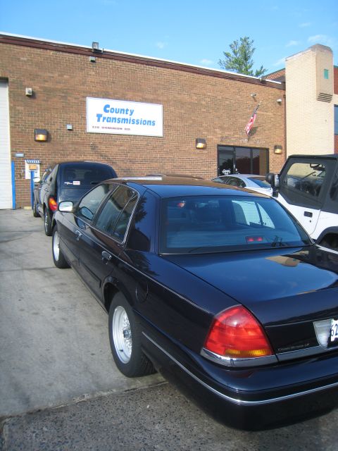 1999 Ford Crown Victoria - A dark sedan is parked in front of a brick building with a sign that reads "County Transmissions".