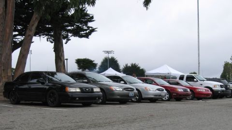 2003 Ford Taurus - A row of Ford Taurus sedans lined up nose-out at an overcast club meet, led by a blacked-out early-90s car on black wheels, followed by gra…