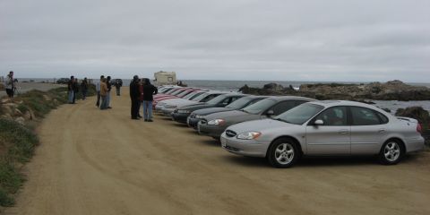 2003 Ford Taurus - A silver 2000s Ford Taurus sedan on five-spoke alloys anchors a long row of Tauruses parked along a dirt bluff at the ocean's edge, with a…