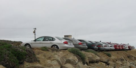 2003 Ford Taurus - Low-angle view from below a rocky bluff of a silver Ford Taurus sedan heading a row of parked Tauruses in silver, dark green, white and red…