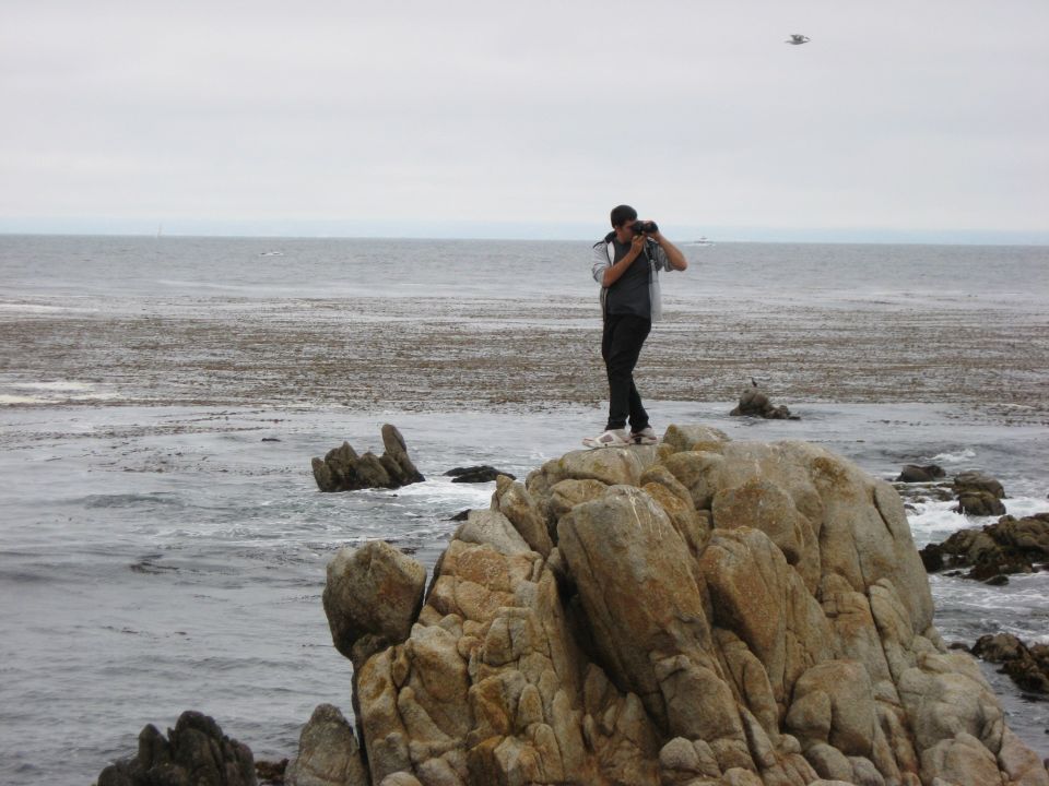 Person on coastal rocks using binoculars to look out at the gray ocean