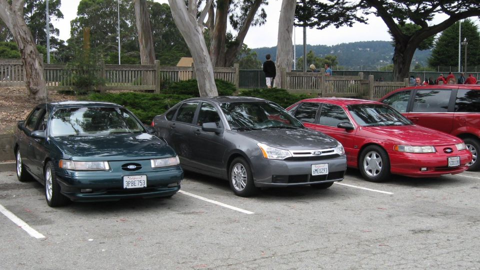 Green and red Ford Taurus sedans with gray Ford Focus parked in a lot