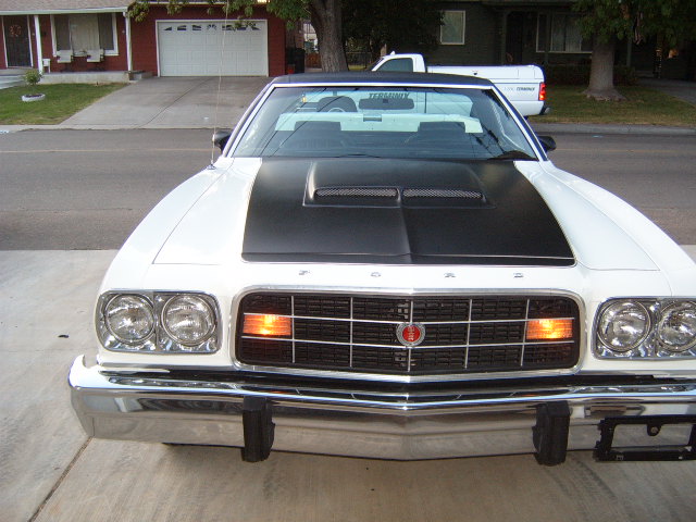 White Ford Ranchero with black hood scoop and grille. White pickup truck in background