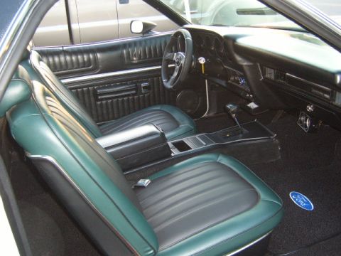 1973 Ford Ranchero - The interior of a 1973 Ford Ranchero features green and black vinyl seats, a center console, and a Ford logo on the floor mat.