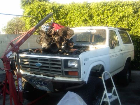1986 Ford Bronco - A white Ford Bronco is undergoing an engine replacement with the help of an engine hoist.