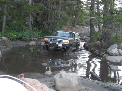 1986 Ford Bronco - This Ford Bronco is navigating a challenging off-road trail with water and mud.
