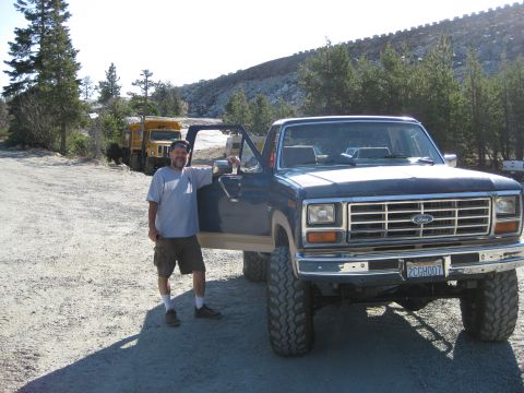 1986 Ford Bronco - Man poses with a lifted Ford pickup truck, with two dump trucks visible behind him.