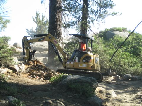 1986 Ford Bronco - A person operates a yellow CAT mini excavator, moving dirt and rocks in a wooded, rocky area.