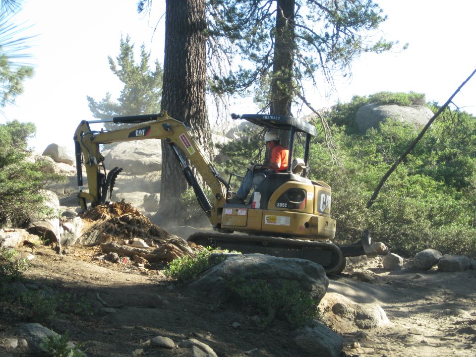 Yellow CAT mini excavator digging dirt and rocks on a sunny day