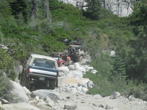1986 Ford Bronco - A 1986 Ford Bronco navigates a rocky off-road trail behind other vehicles.