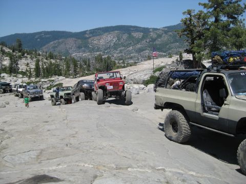 1986 Ford Bronco - A convoy of off-road vehicles traverses a challenging rocky trail under a clear blue sky.