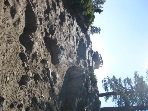 1986 Ford Bronco - An off-road vehicle is precariously positioned on a rocky cliff face under a clear blue sky.