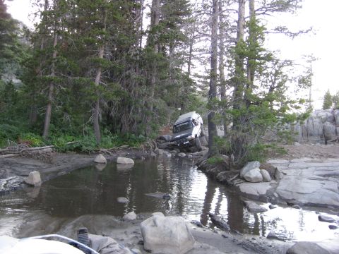 1986 Ford Bronco - A white 1986 Ford Bronco navigates a challenging off-road course with water and rocks.