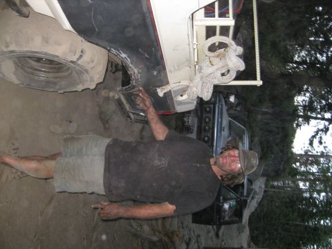 1986 Ford Bronco - Man inspects the undercarriage of a vehicle, with a spare tire and another vehicle in the background.