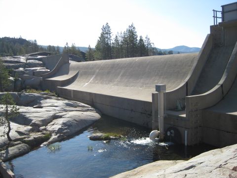 1986 Ford Bronco - A large concrete dam structure is shown with water flowing from a pipe into a pool. The surrounding area is rocky and forested.