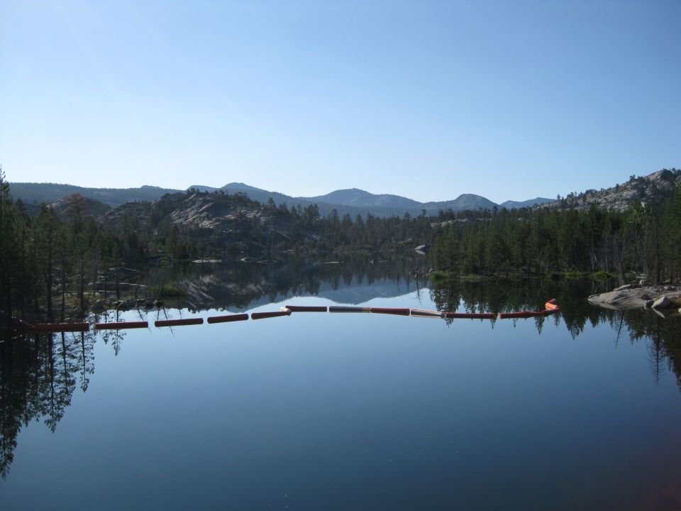 Lake with a line of buoys and forested mountains under a clear blue sky