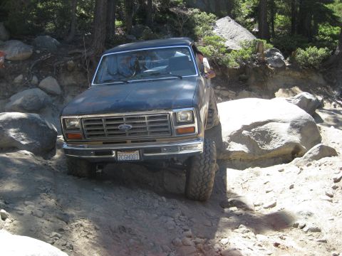 1986 Ford Bronco - This 1980s Ford Bronco is shown tackling a challenging rocky terrain, highlighting its off-road capabilities.