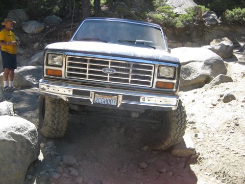 1986 Ford Bronco - 1986 Ford Bronco navigating a rocky off-road path. A person stands by rocks to the left.