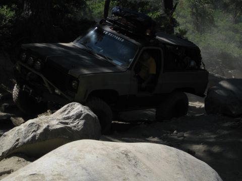 1986 Ford Bronco - Off-road vehicle tackling a challenging rocky path with trees in the background.