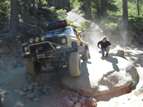 1986 Ford Bronco - This heavily modified off-road vehicle navigates a challenging rocky terrain, kicking up dust.