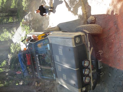 1986 Ford Bronco - An off-road vehicle navigates a challenging rocky path, with two individuals observing the situation.