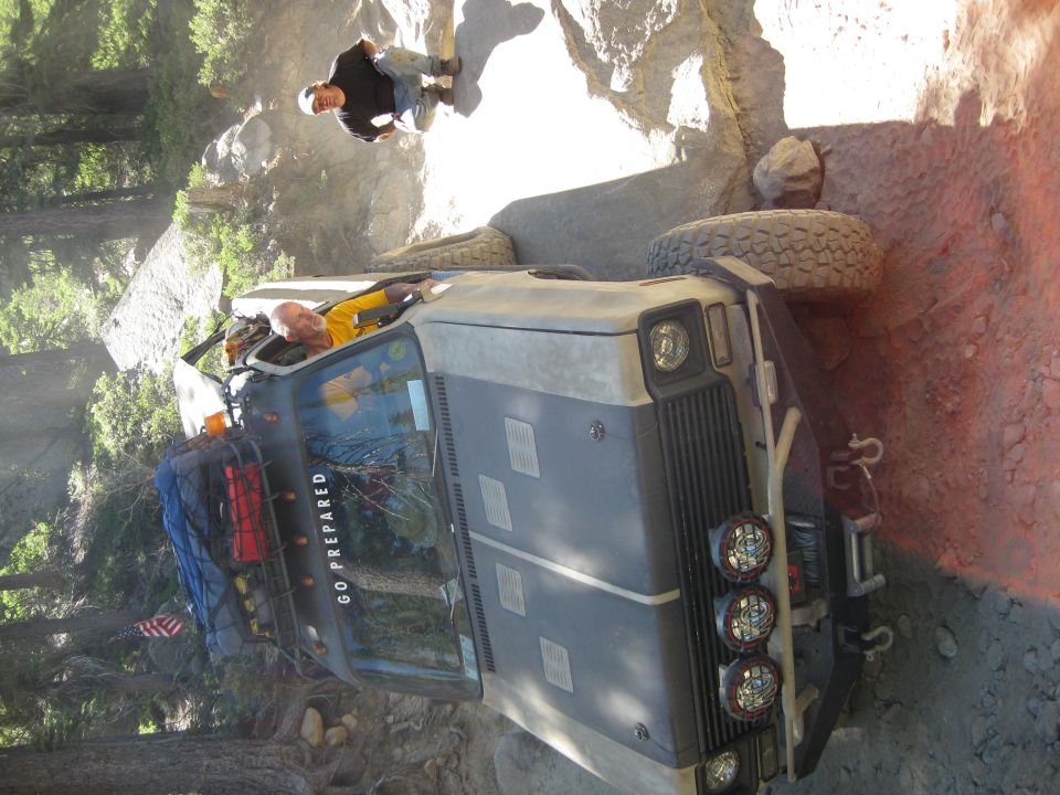 Off-road vehicle stuck on a rocky trail with two people nearby