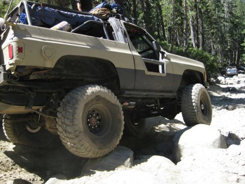 1986 Ford Bronco - This modified SUV tackles a challenging rocky trail in a wooded area.