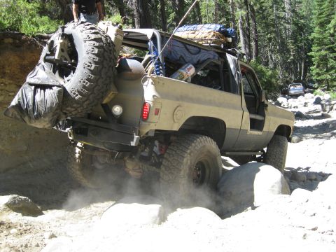 1986 Ford Bronco - Off-road SUV tackling a challenging rocky path in a wooded area.