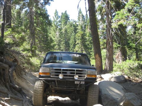 1986 Ford Bronco - This modified Ford Bronco navigates a challenging off-road path through a forest.