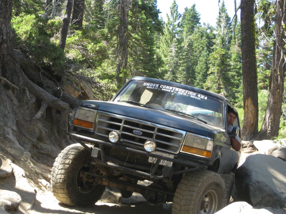Dark blue 1992 Ford Bronco navigating rocky terrain with "Under Construction 4x4" sticker on windshield