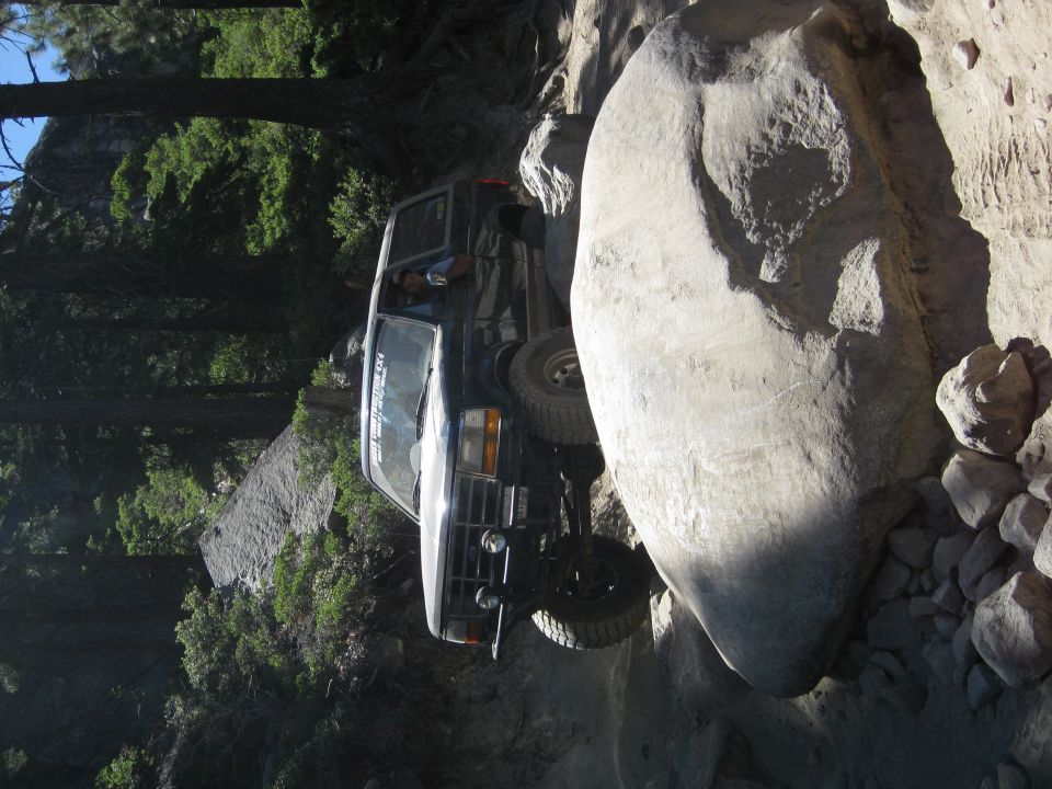 Black SUV navigating a tight spot between large rocks on a trail. Driver visible