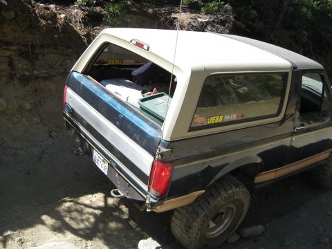 1986 Ford Bronco - This 1986 Ford Bronco is seen from the rear, with a black and tan exterior, parked on a dirt trail.