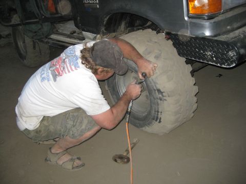 1986 Ford Bronco - Man airing up a large off-road tire on a vehicle with a tool.