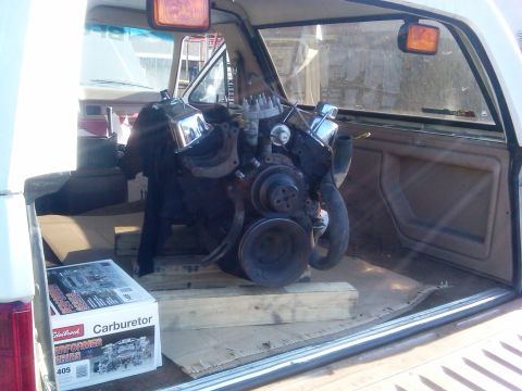 1986 Ford Bronco - A vehicle interior shows an engine and a new carburetor box being transported.