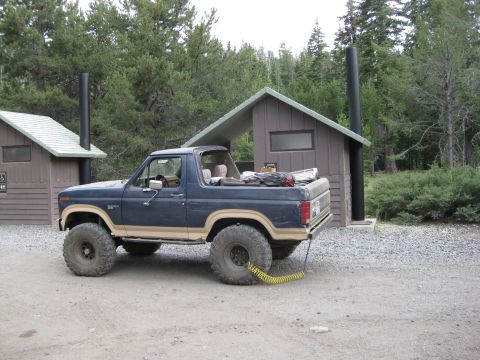 1986 Ford Bronco - Ford Bronco parked in a wooded area near a restroom facility.
