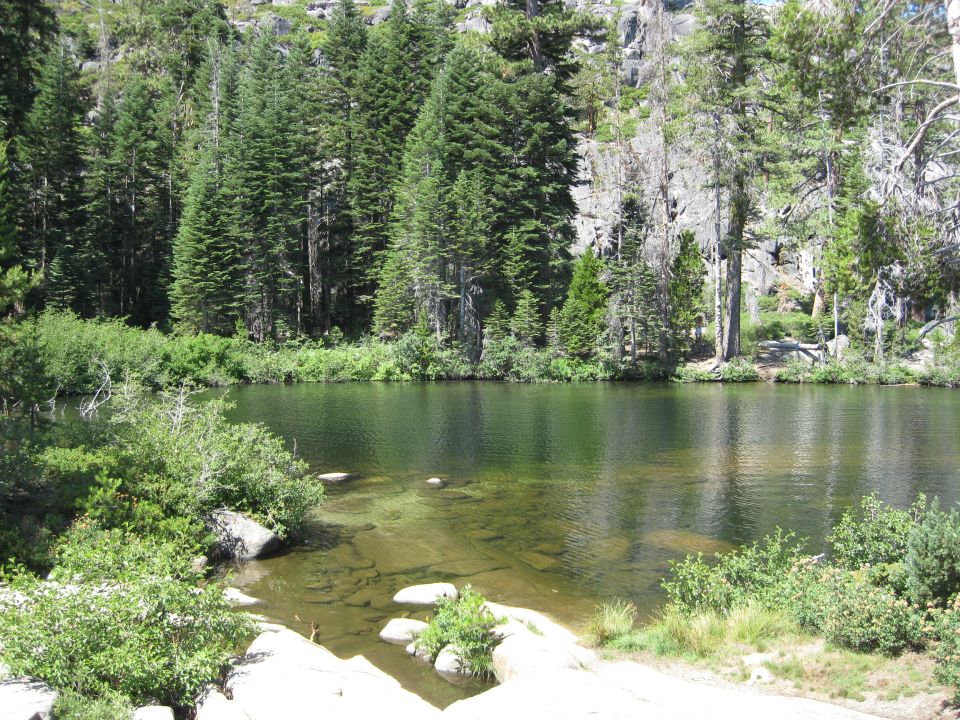 Lake with clear water and rocky shore, surrounded by pine trees and granite cliffs