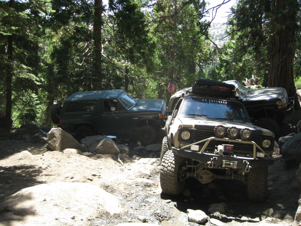1986 Ford Bronco and another off-road vehicle navigating a rocky trail in a forest