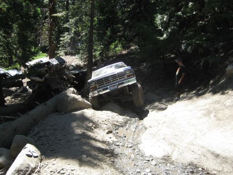 1986 Ford Bronco - A white Ford Bronco is seen off-roading on a challenging dirt path with a person standing nearby.