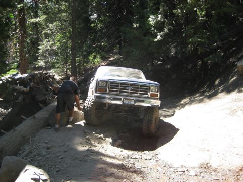 1986 Ford Bronco - Ford Bronco tackling a difficult off-road path in a forest setting. The vehicle appears to be from the early 1980s.